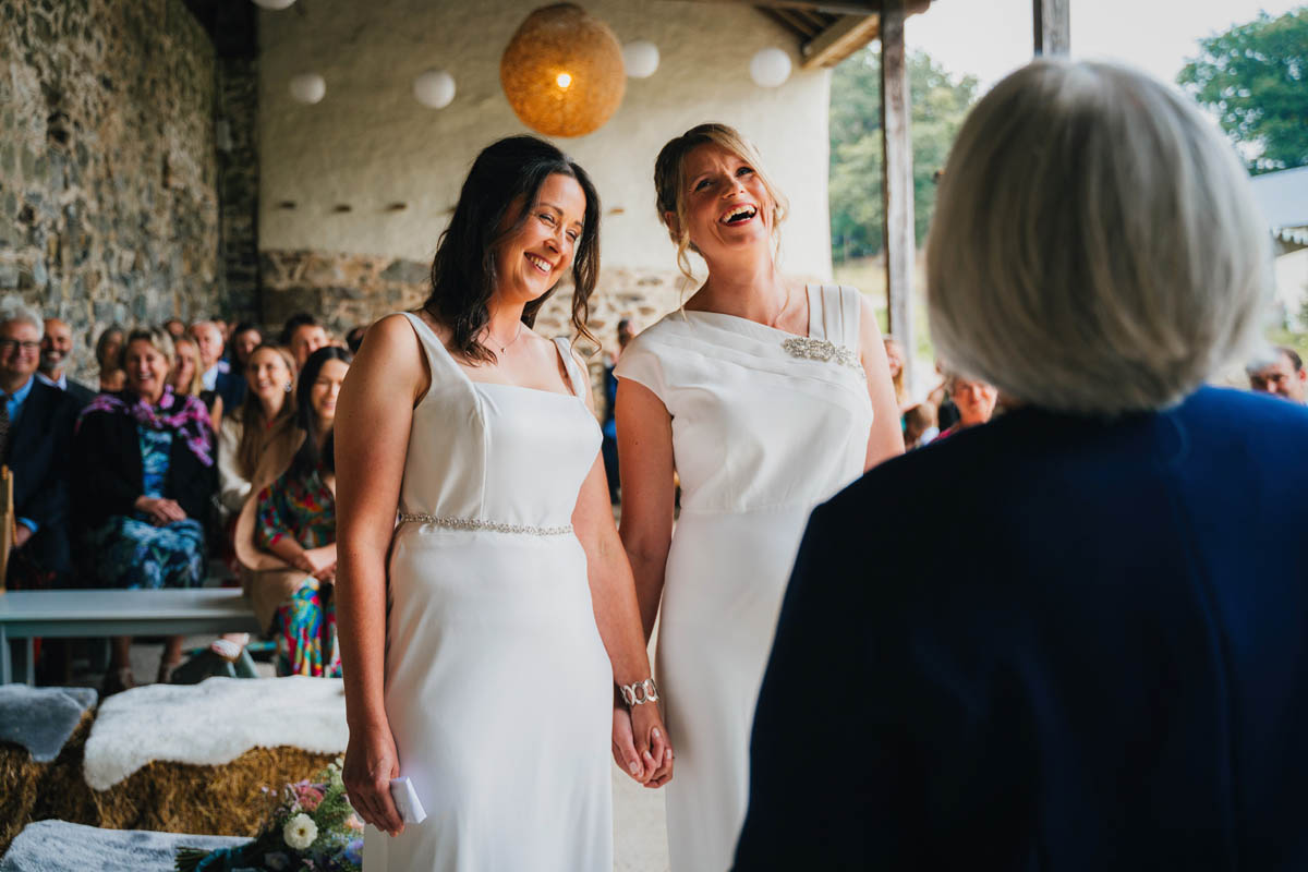 two brides hold hands and laugh with the celebrant