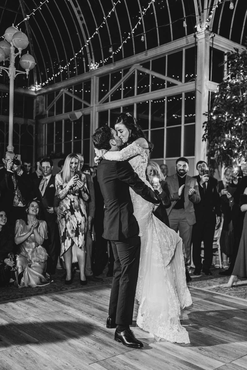 a man picks up his bride sa guests laugh and smile behind them on the dancefloor