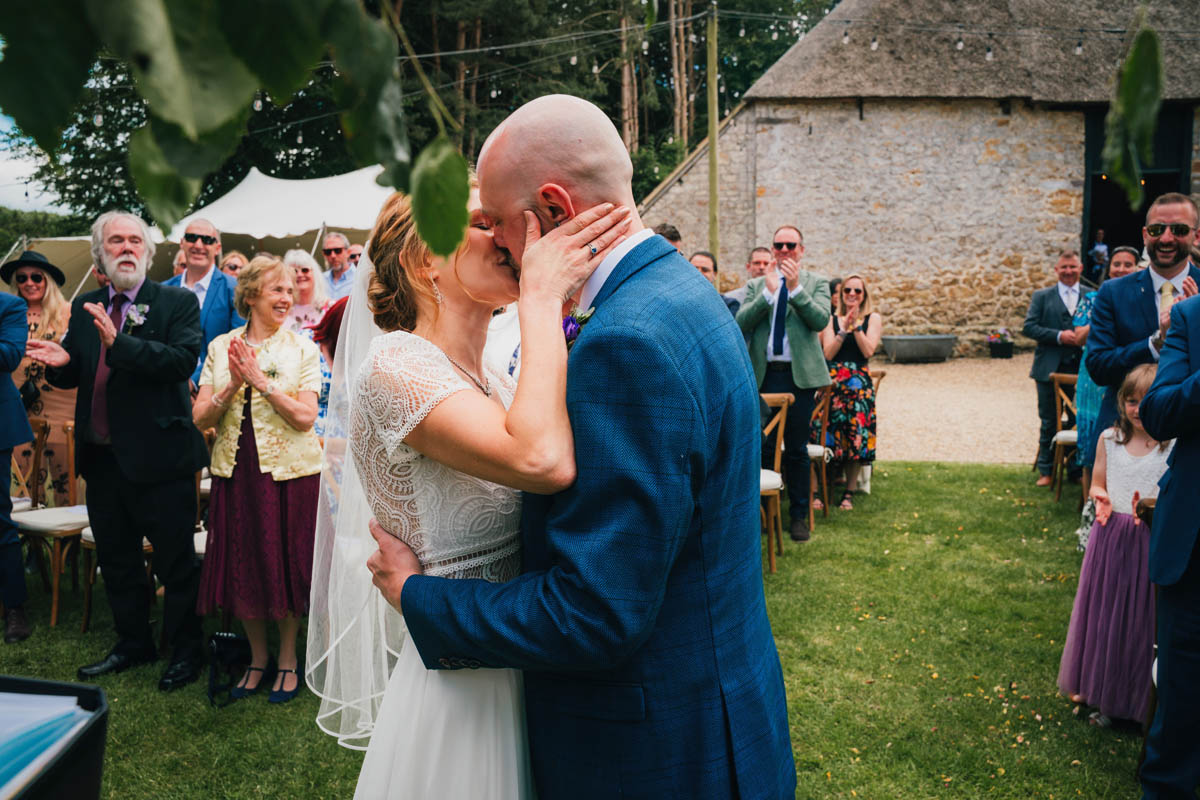 a couple kiss as their guests smile and clap behind