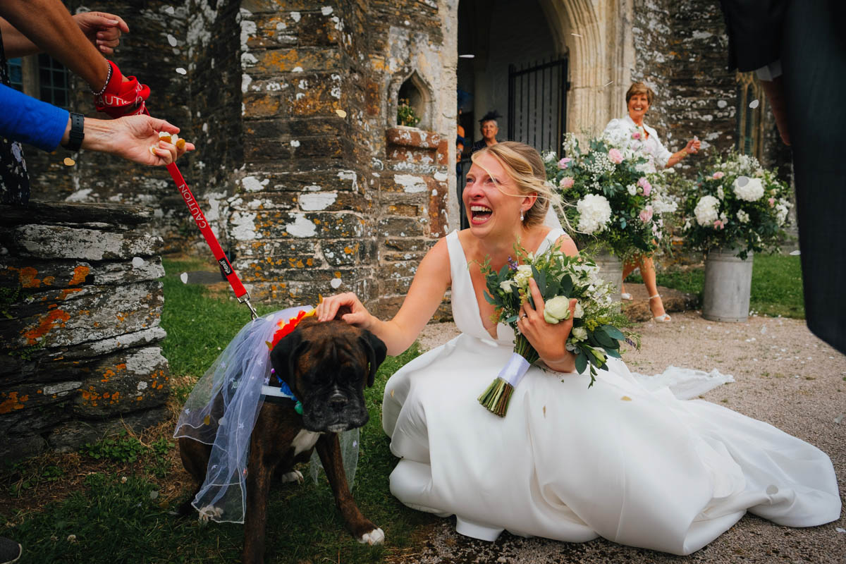 a woman laughs as her dog greets her in a wedding veil