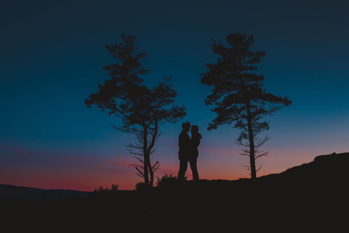 a silhouette of a couple hugging between two trees