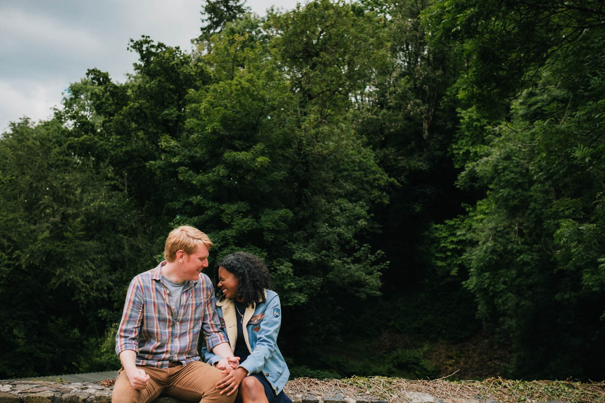 a couple laugh together as they sit on a wall