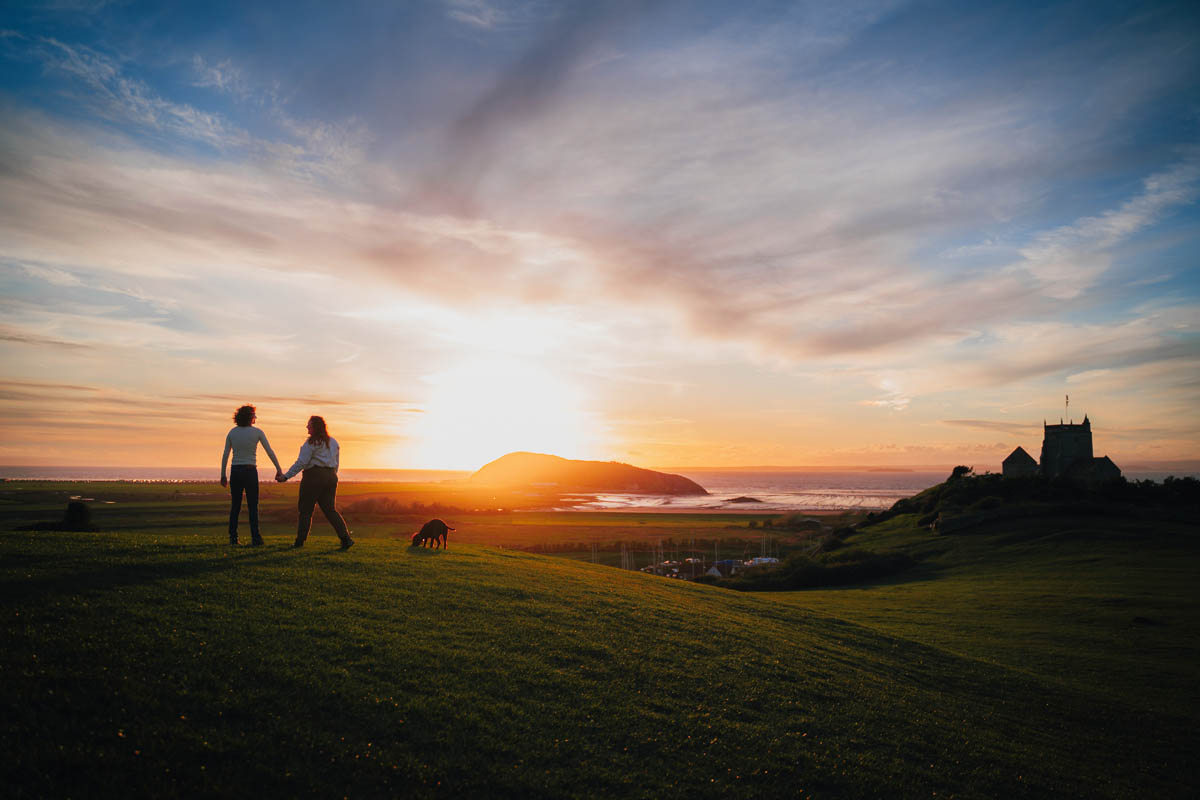 a couple walk along the hills with their dog at sunset