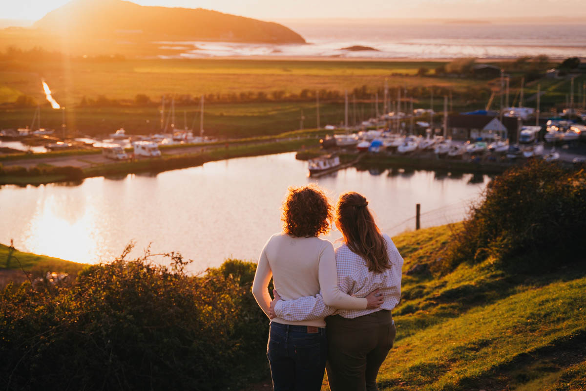 two women hug one another as they look out at the setting sun