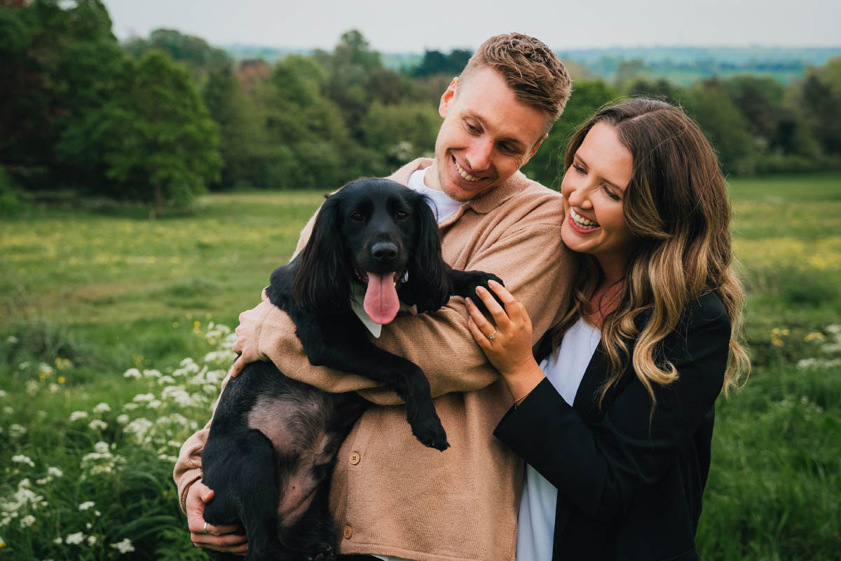 a couple smile and hug their black cocker spaniel