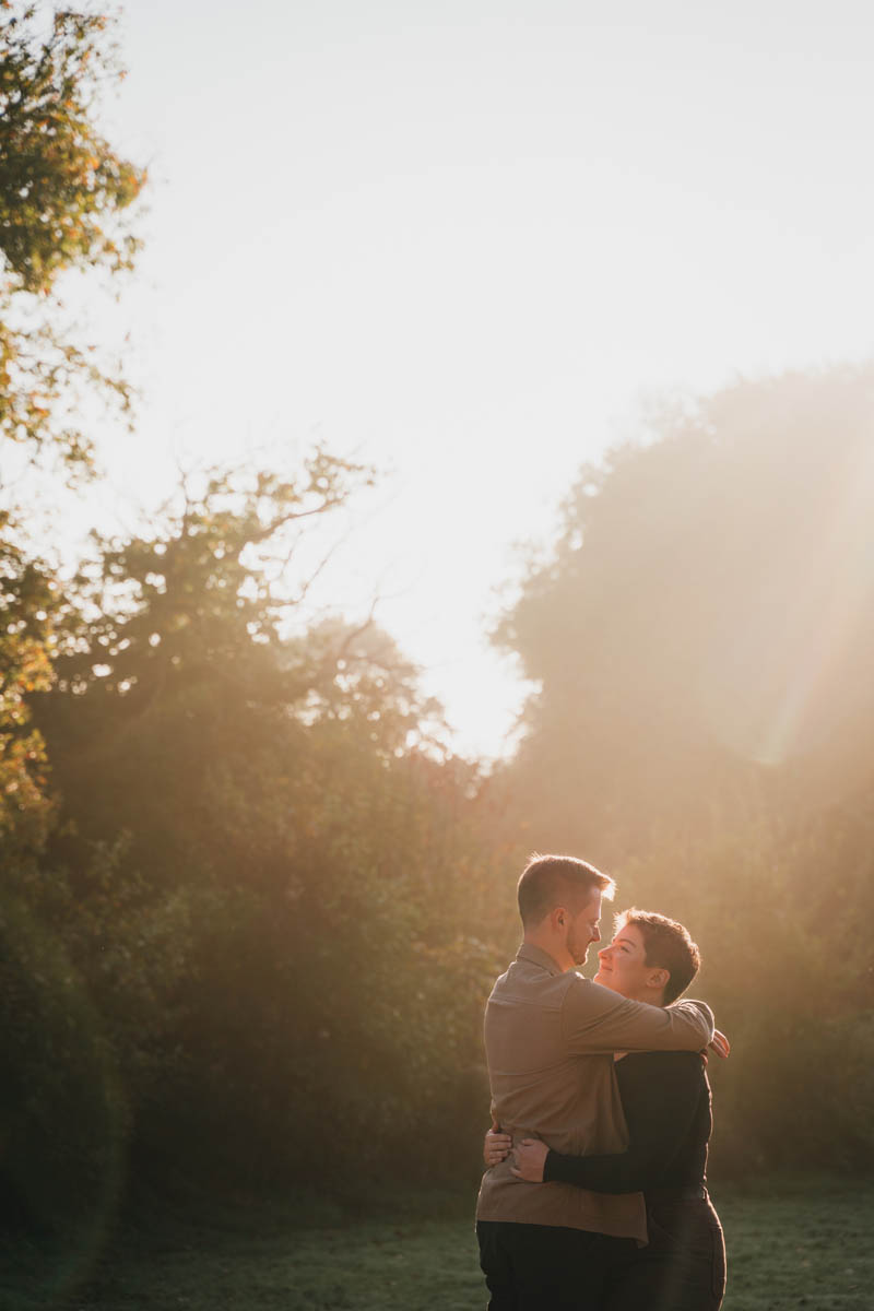 a newly-engaged couple hug through sun flare