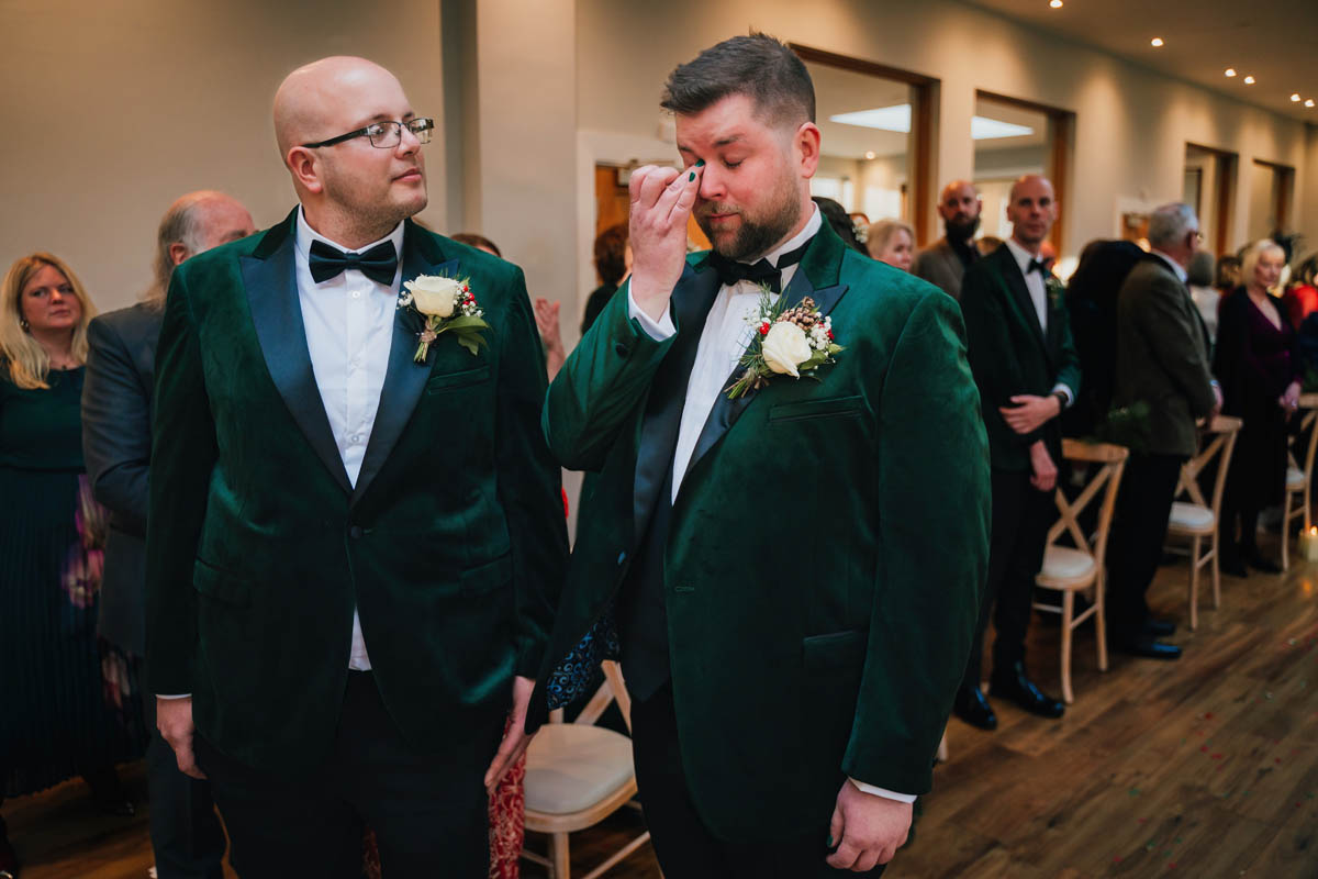 a groom wipes away a tear as he waits for his bride