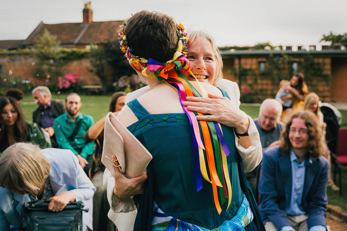 a person hugs another whilst wedding guests watch behind