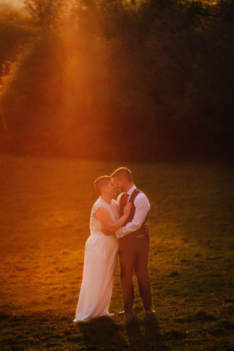 a couple hug one another and kiss as a mean of golden light showers down on them at Ashton Court, Bristol