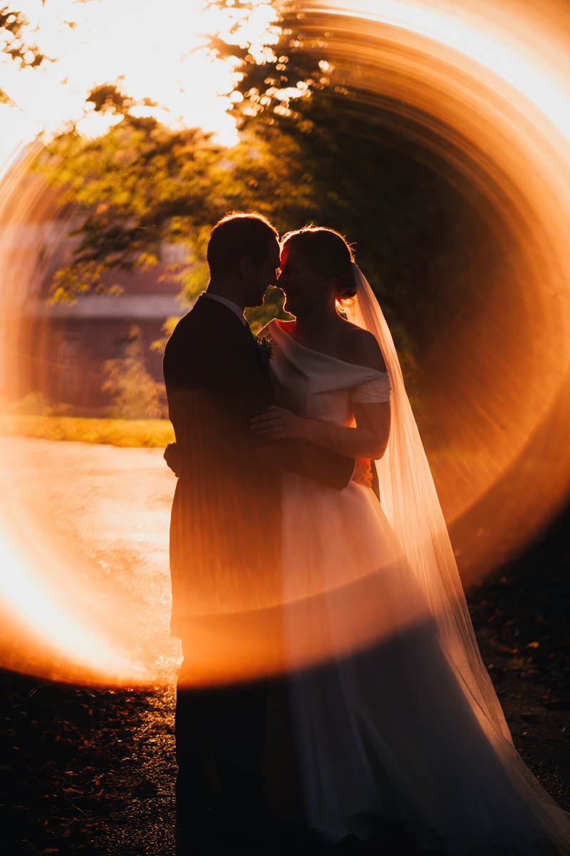 a couple kiss at golden hour on their wedding day with a ring of fire surrounding them