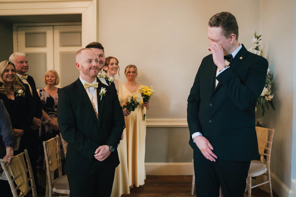 the groom wipes away a tear as his bride walks down the aisle