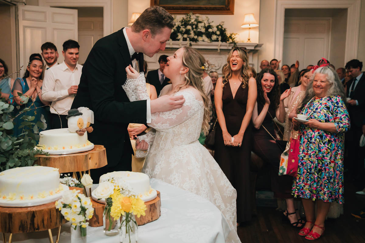 guests laugh as the couple feed each other a slice of cake
