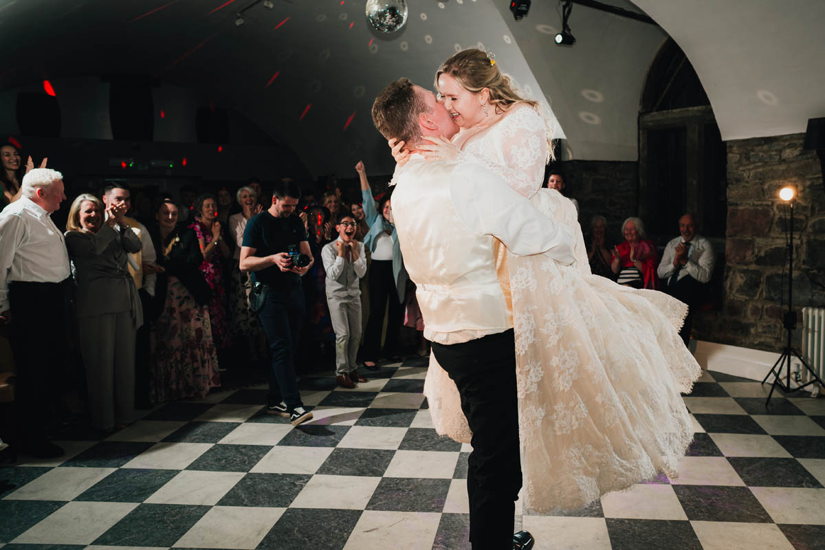 a bride and groom kiss during their first dance, wedding guests cheer behind