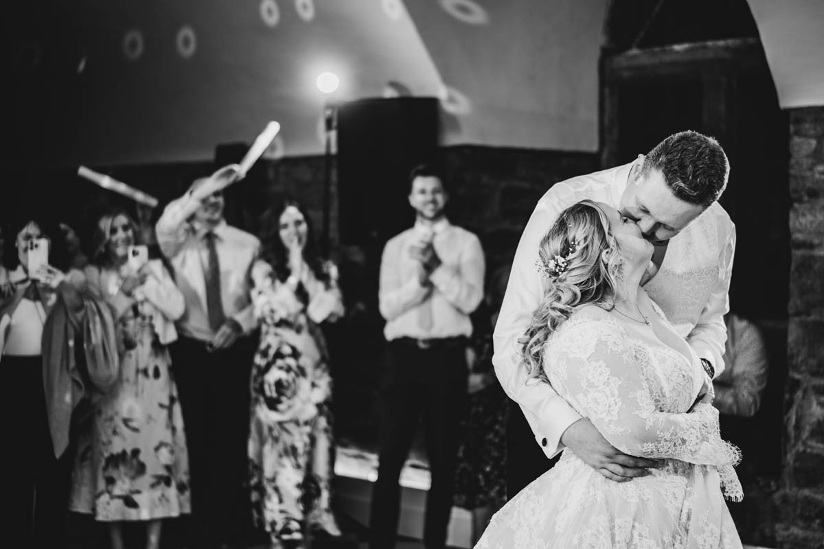 a bride ansd groom kiss on the dancefloor with wedding guets behind