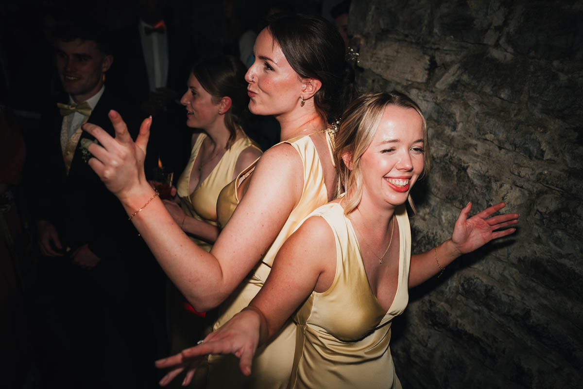 three bridesmaids wearing yellow dresses dance, they are lit with flash